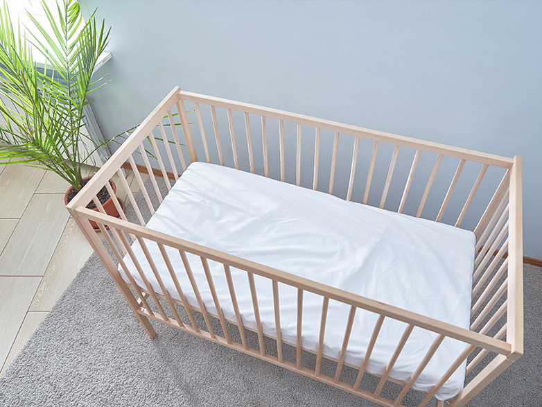 Holzbabybett mit weißer Matratze in einem hellen Kinderzimmer