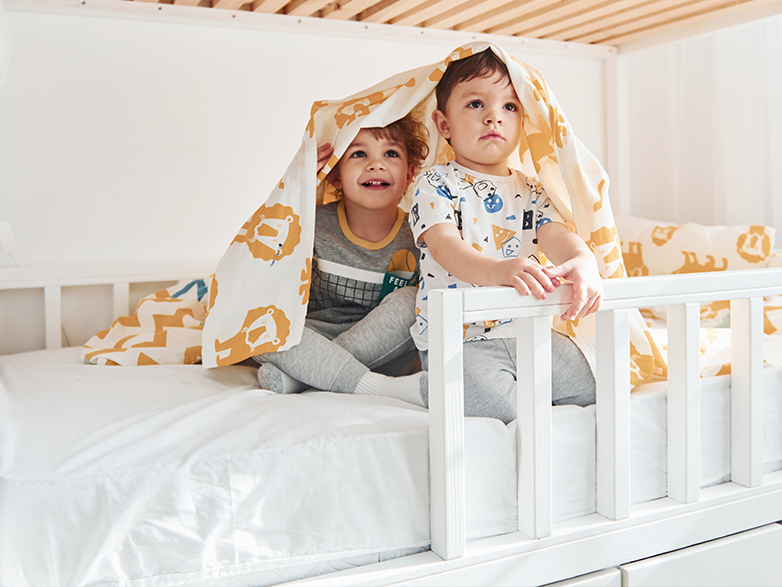 Zwei Kinder sitzen lachend auf der Matratze im Hausbett
