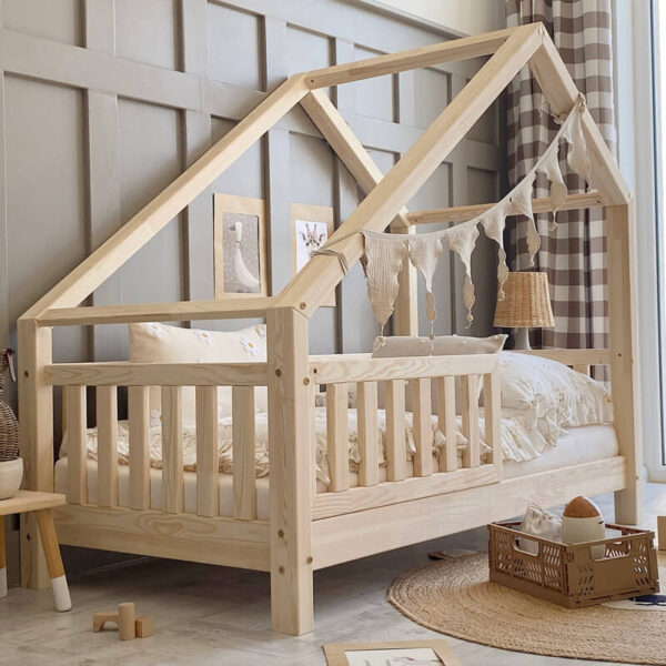 Ein Kinderholzbett mit Schutzgitter in einem beigen Zimmer mit kariertem Vorhang und braunem Spielzeug